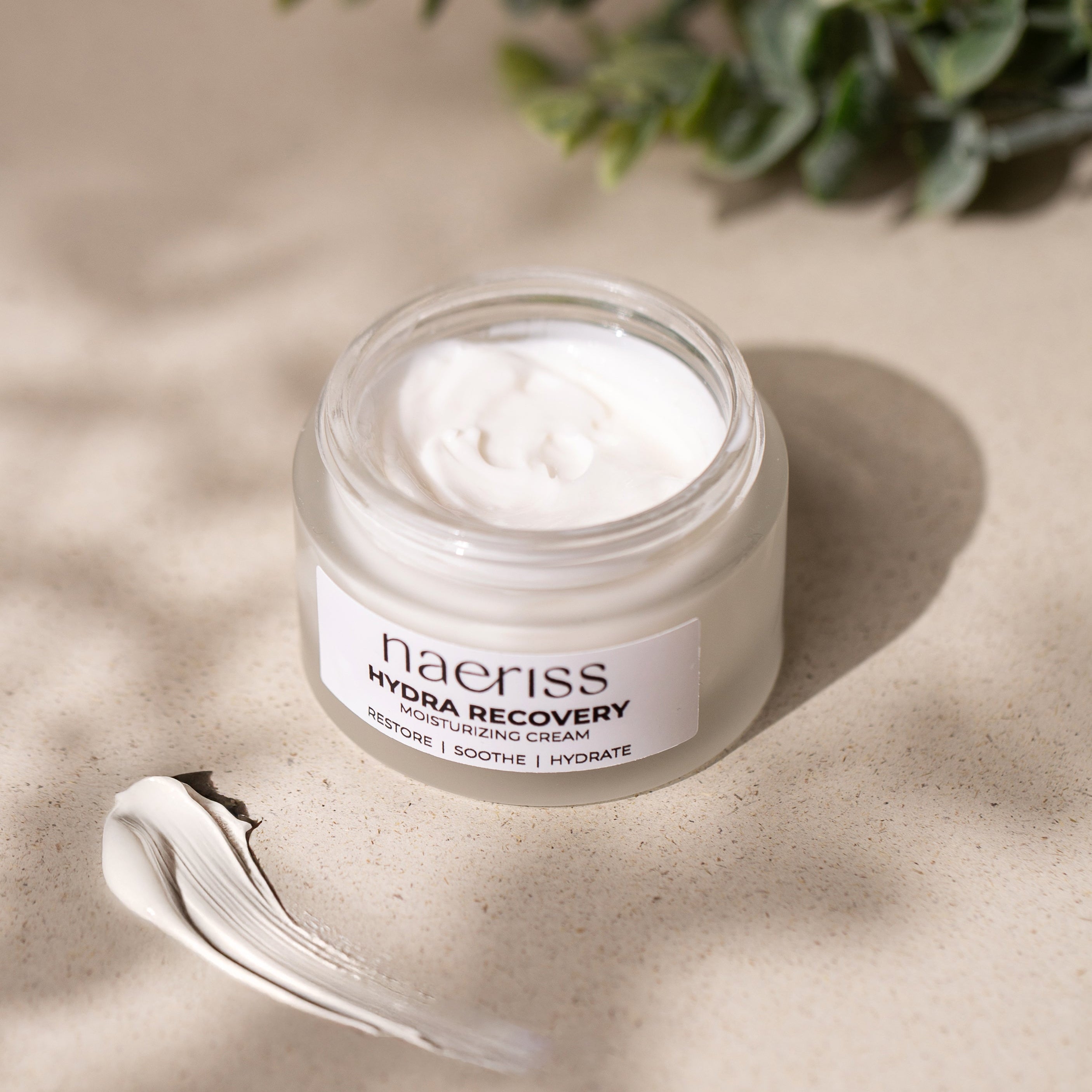Jar of naeriss Hydra Recovery cream on a beige surface with a plant in the background
